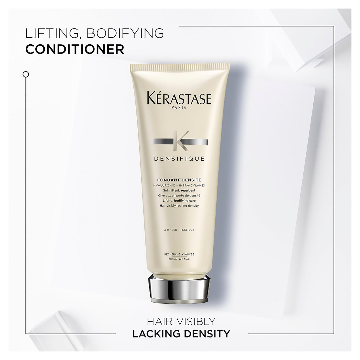 A sleek tube of Densifique Fondant Densité 200ml by Kerestase, in elegant white and silver, is beautifully displayed on a minimalist white backdrop. The description highlights its nourishing qualities as well as its ability to lift and add body to hair that lacks visible density.