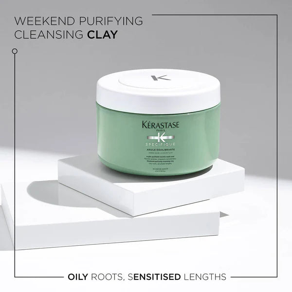 A green jar of Specifique Argile Équilibrante 250ml from Kerestase is displayed on a white platform against a light gray background. Although the product description appears to be incomplete, it's evident that this item addresses oily roots and sensitized lengths.